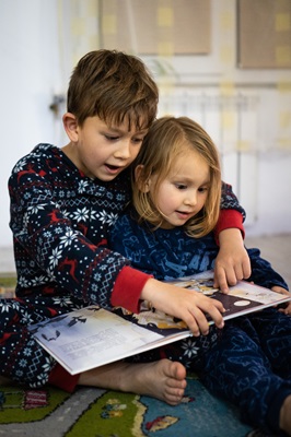 two children in pajamas reading together and snuggling.